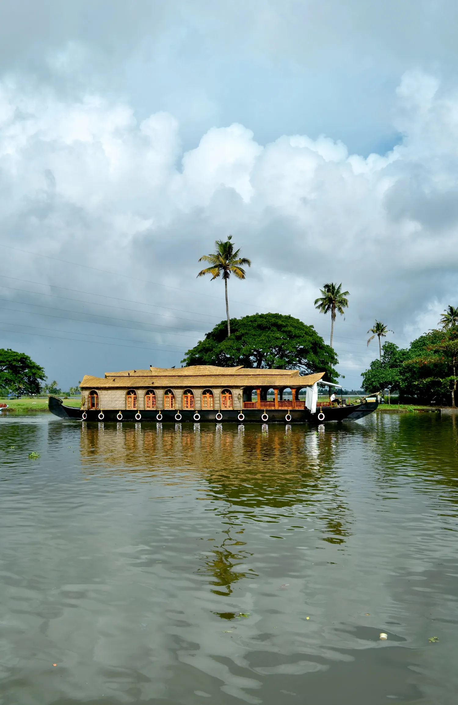 A kettuvallam houseboat moving through a palm-lined channel of the Kerala backwaters